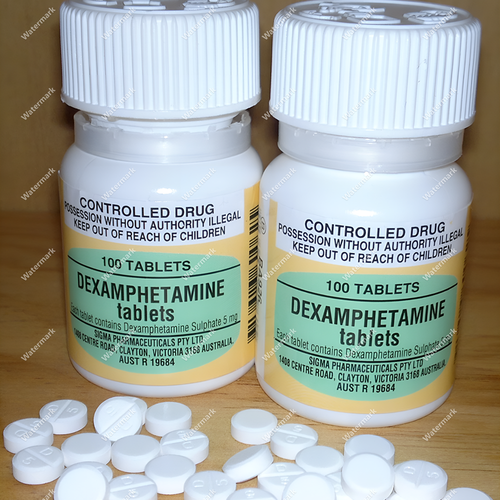 Два белых флакона Дексамфетамина (Dexamphetamine) по 5 мг от австралийского производителя Sigma Pharmaceuticals. Рядом рассыпаны маленькие круглые таблетки белого цвета. На этикетке видна надпись Controlled Drug.